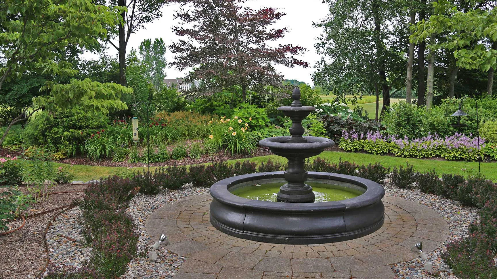 Black water fountain feature surrounded by a paved walkway and foliage in Lansing, MI.