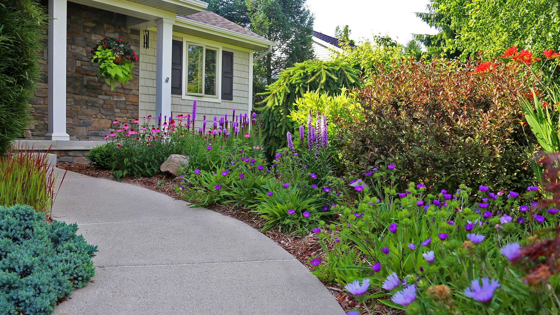 Paved walkway surrounded by flowers leading to front door of a home in Haslett, MI.
