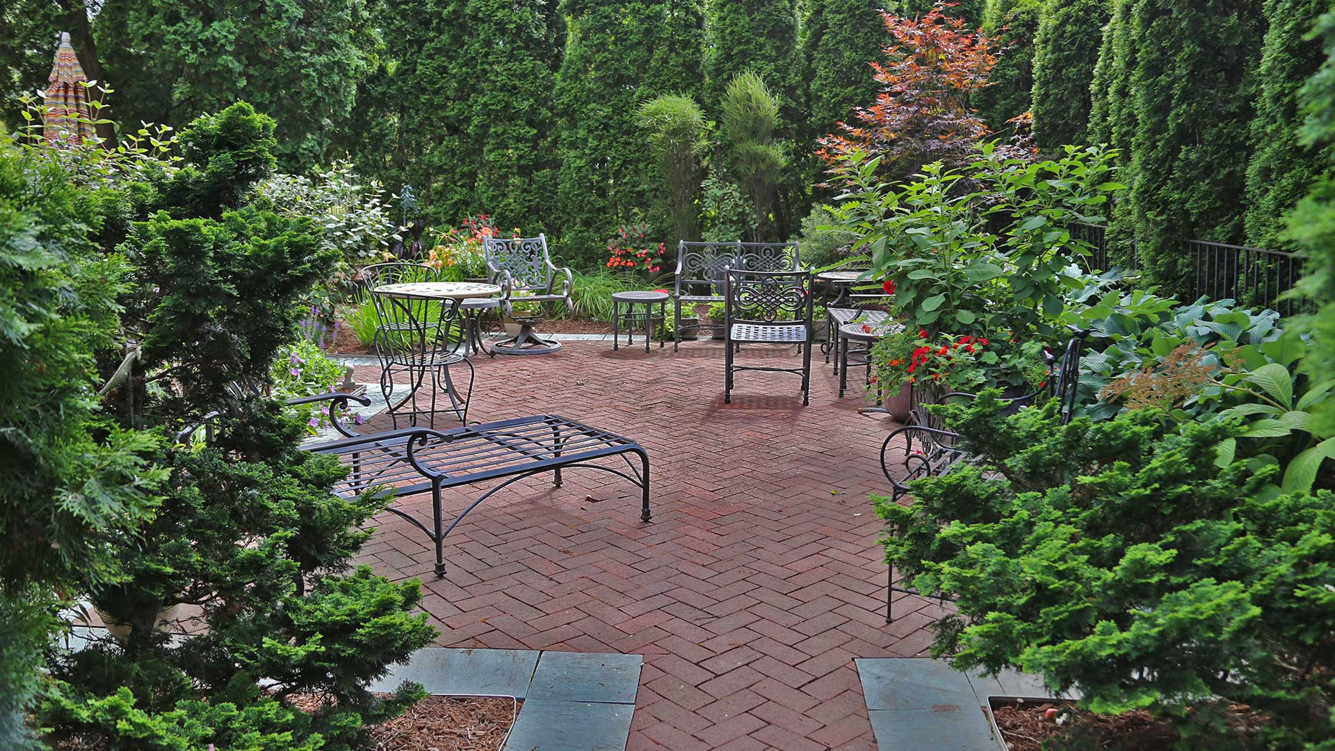 Patio and walkway with black furniture surrounded by green foliage in Dewitt, MI.