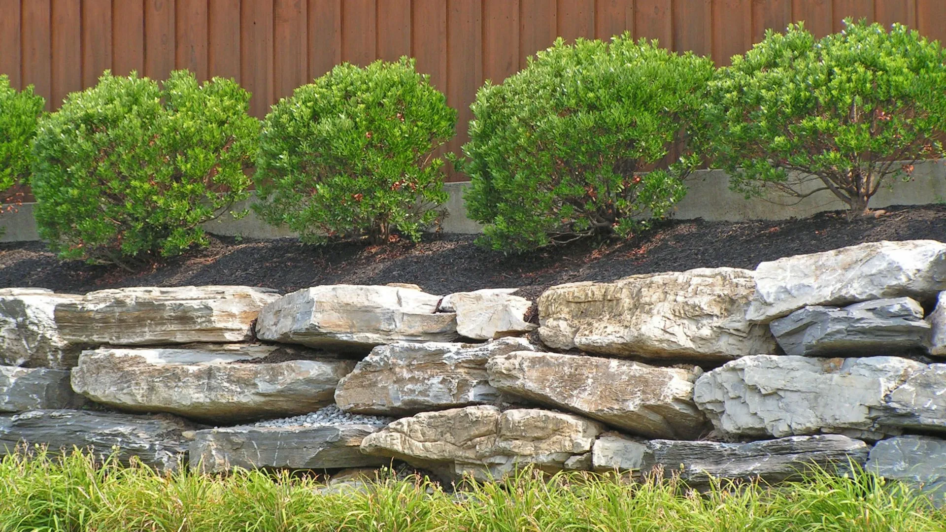 A stone retaining wall surrounding round bushes in Okemos, MI.