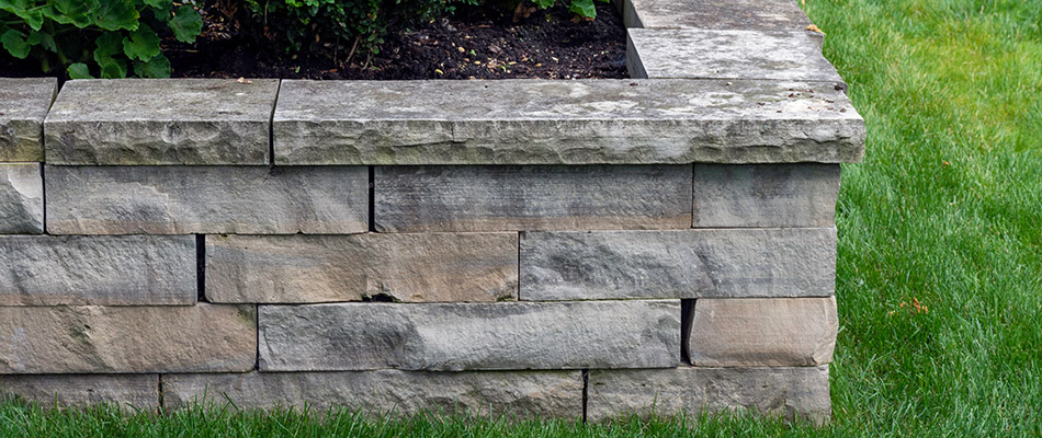 A grey stone retaining wall surrounding a raised landscape bed in Okemos, MI.