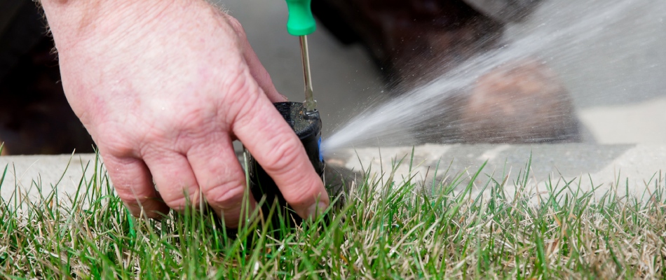 Professional with tool repairing faulty irrigation system in Lansing, MI.