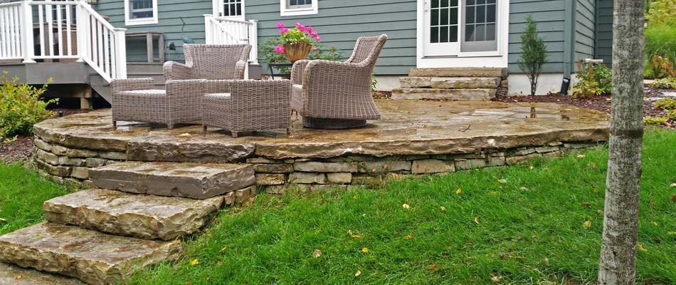 A rounded paved stone patio with steps and wicker furniture in Williamston, MI.